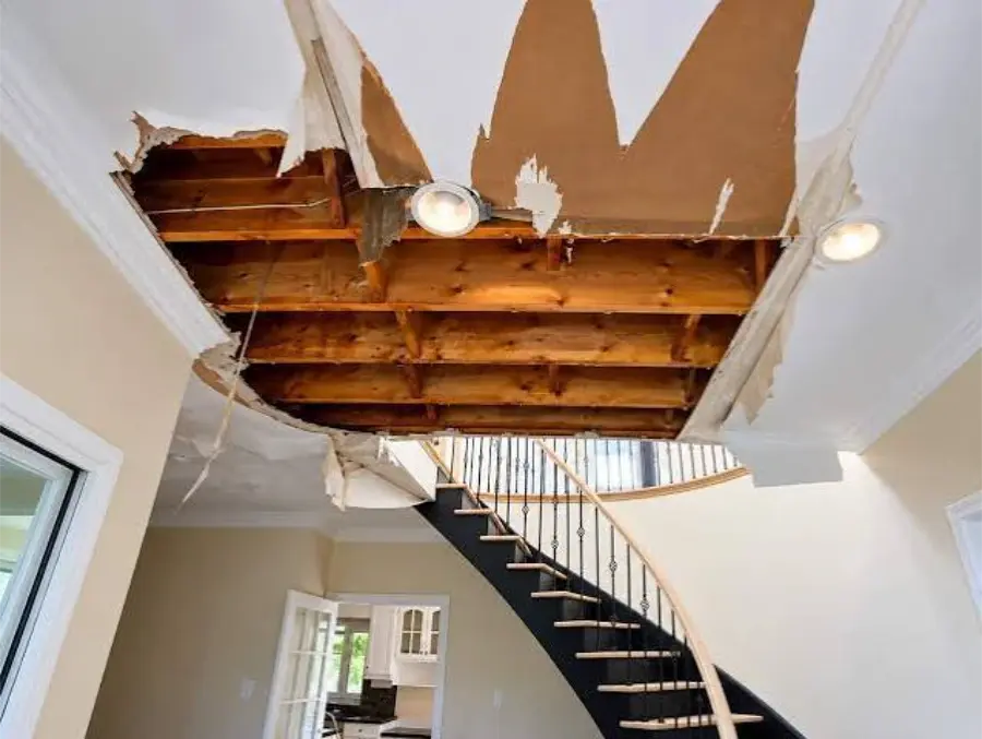 Water-damaged ceiling opened up to the wooden joists above a staircase, ready for drying and rebuilding