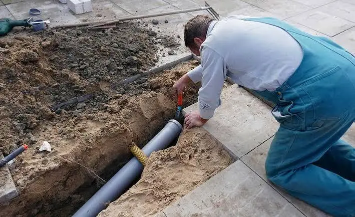 Plumber fitting a new PVC sewer pipe in an open trench to fix the cause of a sewer backup